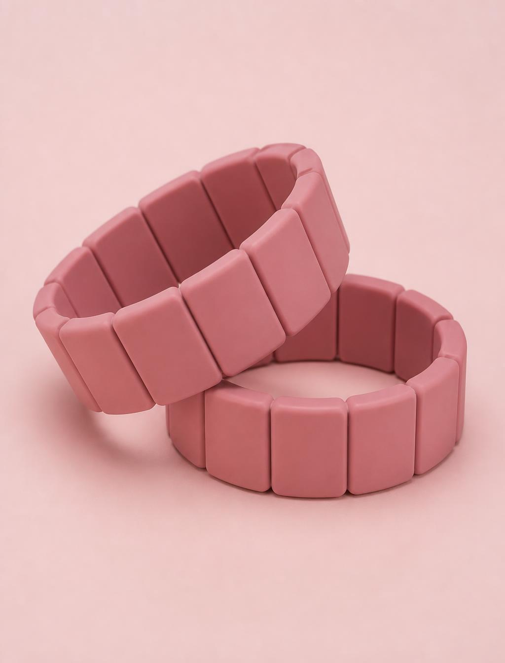 The Orbit pair — two weighted wrist bangles in Rose, on a plain blush ground
